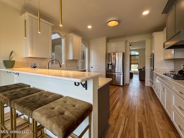 kitchen featuring appliances with stainless steel finishes, arched walkways, a kitchen breakfast bar, a peninsula, and wood finished floors