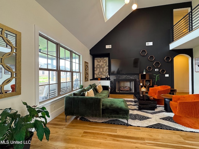 living area featuring high vaulted ceiling, wood finished floors, a premium fireplace, arched walkways, and a skylight
