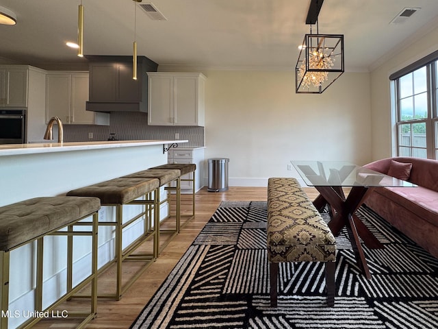 kitchen featuring stainless steel oven, ornamental molding, light countertops, tasteful backsplash, and hanging light fixtures