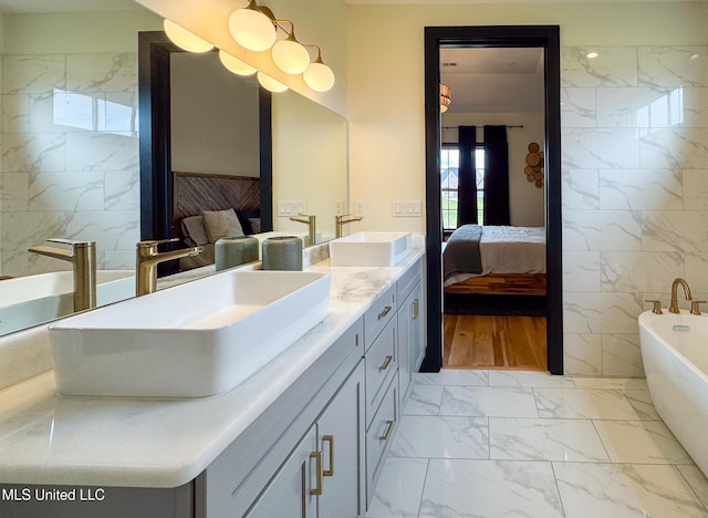 ensuite bathroom featuring marble finish floors, tile walls, double vanity, and a freestanding tub