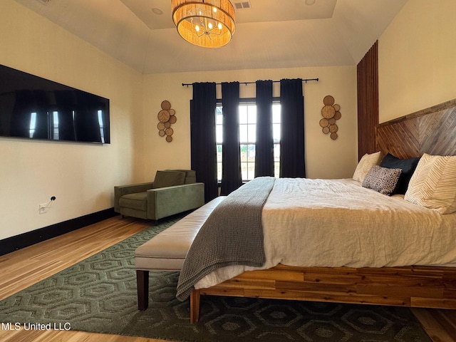 bedroom featuring a chandelier, wood finished floors, and a raised ceiling