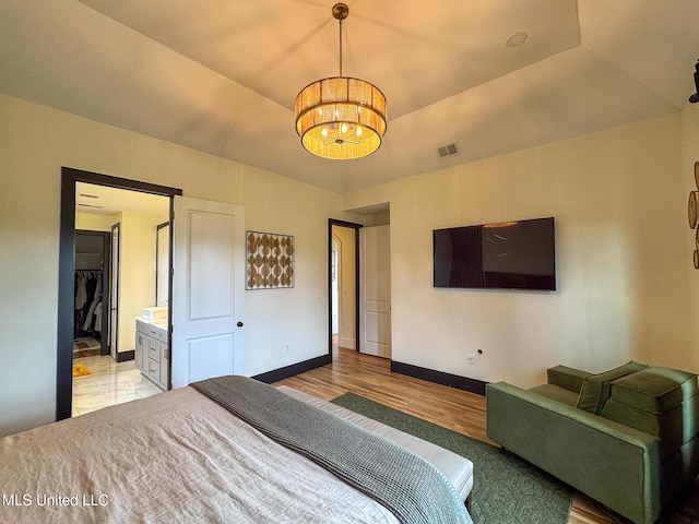 bedroom featuring a chandelier, light wood-style flooring, baseboards, ensuite bathroom, and a raised ceiling