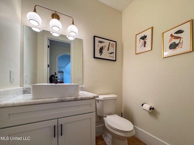half bathroom featuring vanity, toilet, and baseboards