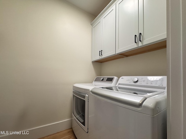 clothes washing area with washing machine and clothes dryer, cabinet space, light wood-type flooring, and baseboards