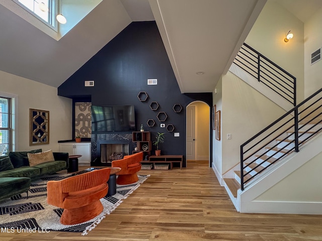 living room with high vaulted ceiling, arched walkways, wood finished floors, stairway, and a premium fireplace