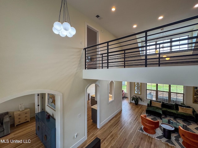 living area with arched walkways, wood finished floors, a high ceiling, recessed lighting, and a chandelier