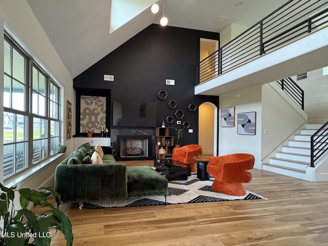 living area featuring high vaulted ceiling, wood finished floors, stairs, a fireplace, and arched walkways