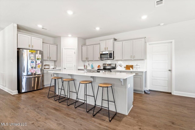 15380 Woodmanse Way, Diberville, MS 39540 - kitchen with stainless steel appliances, a breakfast bar area, dark wood-type flooring, a kitchen island with sink, and tasteful backsplash