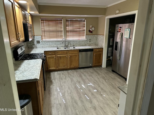 kitchen featuring tasteful backsplash, sink, ornamental molding, light hardwood / wood-style floors, and stainless steel appliances