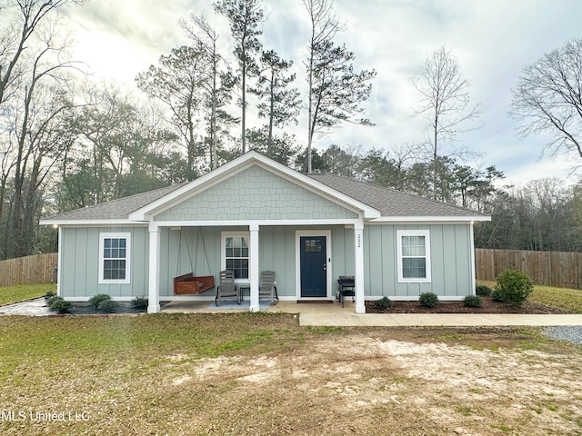 view of front of home with roof with shingles, a front lawn, board and batten siding, and fence