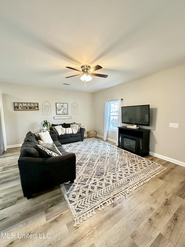 living room with visible vents, ceiling fan, light wood-style flooring, and baseboards