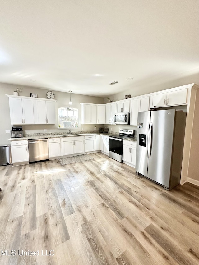 kitchen with hanging light fixtures, light wood finished floors, white cabinetry, and stainless steel appliances