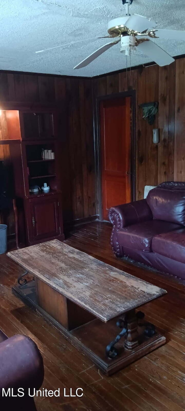 living room featuring a textured ceiling, wooden walls, wood-type flooring, and a ceiling fan
