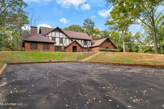 tudor-style house with brick siding, a front yard, stairs, a chimney, and a shingled roof