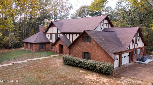 tudor home with a garage, a front lawn, and central AC unit