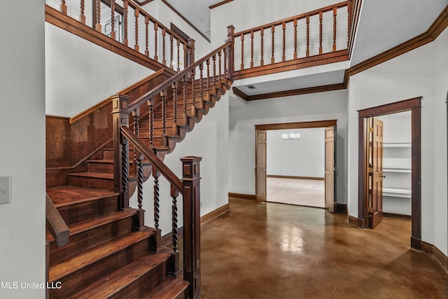 stairway with a towering ceiling, ornamental molding, and concrete flooring