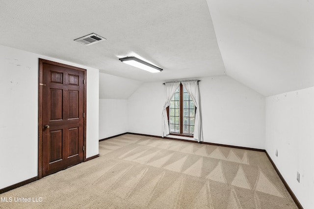 additional living space featuring a textured ceiling, vaulted ceiling, and light colored carpet