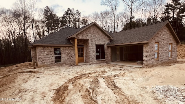 view of front of property featuring a patio, a garage, brick siding, and roof with shingles