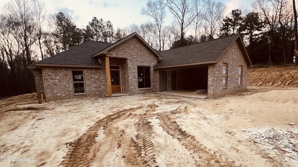 view of front of house with a garage, brick siding, a patio area, and a shingled roof