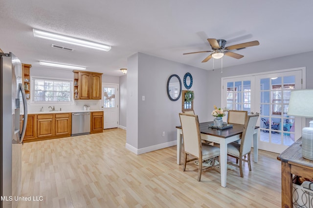 dining space with light wood-style flooring, baseboards, a textured ceiling, visible vents, and a ceiling fan