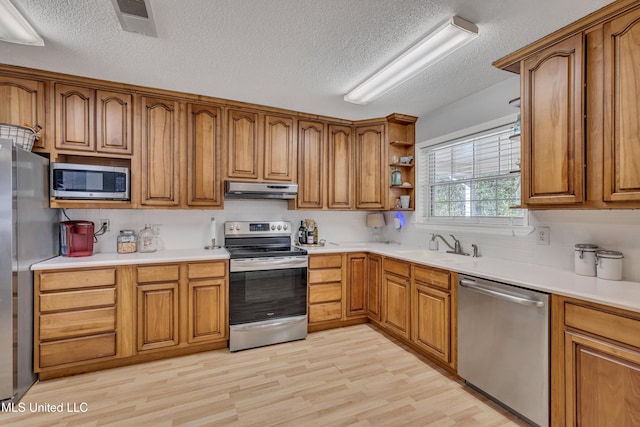 kitchen with brown cabinetry, under cabinet range hood, and stainless steel appliances