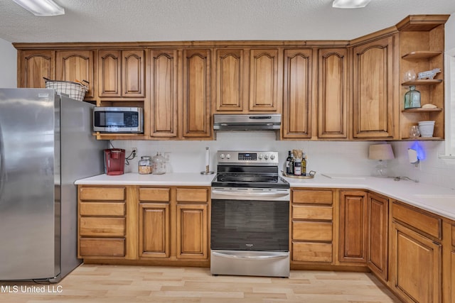 kitchen featuring light wood finished floors, brown cabinets, under cabinet range hood, and appliances with stainless steel finishes