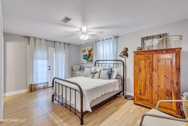 bedroom featuring baseboards, a textured ceiling, visible vents, and light wood-type flooring