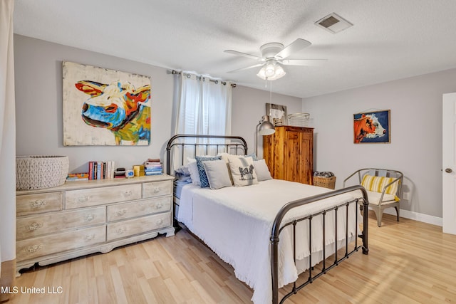bedroom with light wood-type flooring, baseboards, a textured ceiling, visible vents, and a ceiling fan