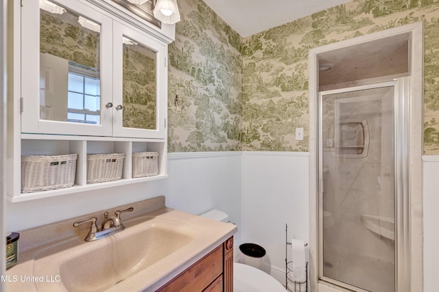 full bath with a wainscoted wall, wallpapered walls, toilet, and a stall shower
