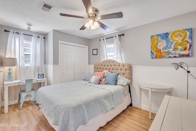 bedroom with a wainscoted wall, light wood-style floors, and a textured ceiling