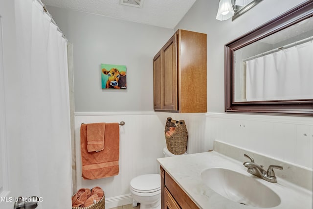 bathroom with toilet, vanity, a textured ceiling, and wainscoting