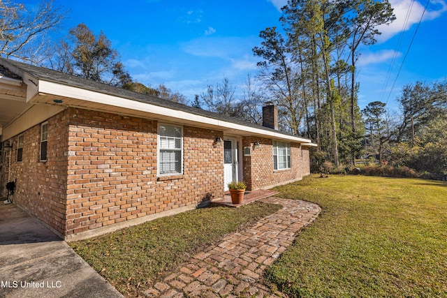 single story home featuring a chimney, a front yard, and brick siding