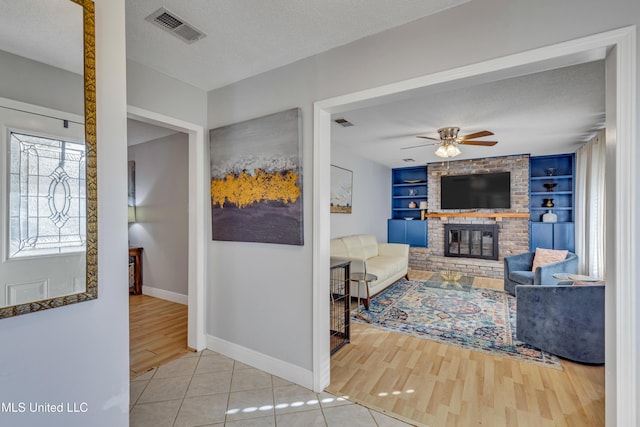 living room featuring built in features, a ceiling fan, a textured ceiling, and visible vents