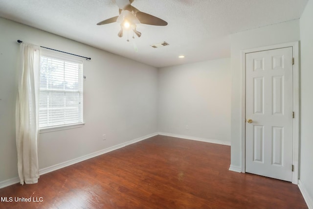 unfurnished room with a textured ceiling, wood finished floors, a ceiling fan, visible vents, and baseboards