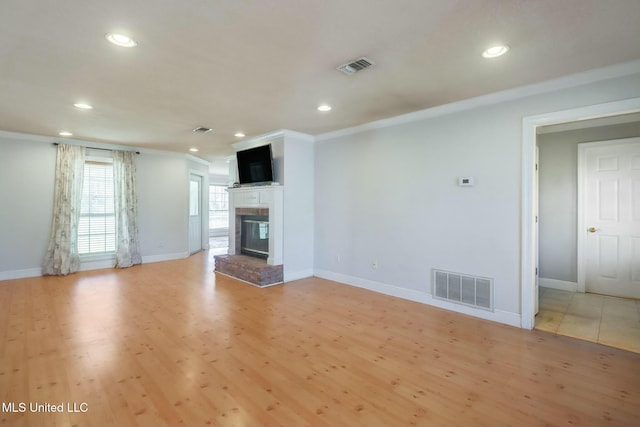 unfurnished living room featuring a brick fireplace, baseboards, visible vents, and light wood finished floors