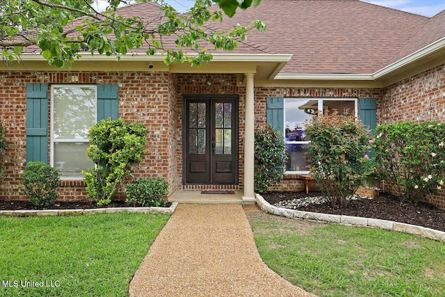 view of exterior entry featuring roof with shingles, brick siding, french doors, and a lawn