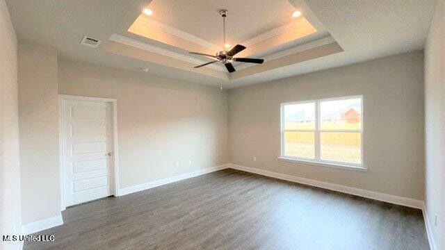 empty room featuring crown molding, a raised ceiling, and dark wood finished floors