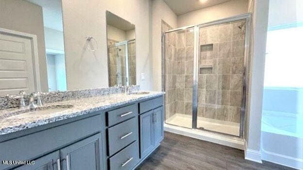 full bathroom with double vanity, wood finished floors, a stall shower, and a sink