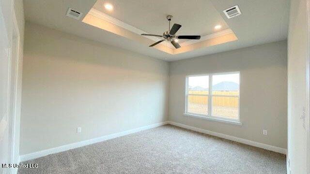 empty room with a tray ceiling, light colored carpet, visible vents, ornamental molding, and baseboards