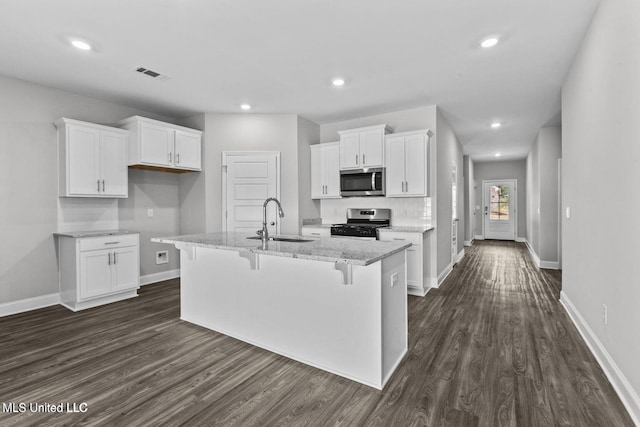 kitchen featuring stainless steel appliances, a sink, white cabinetry, light stone countertops, and a center island with sink