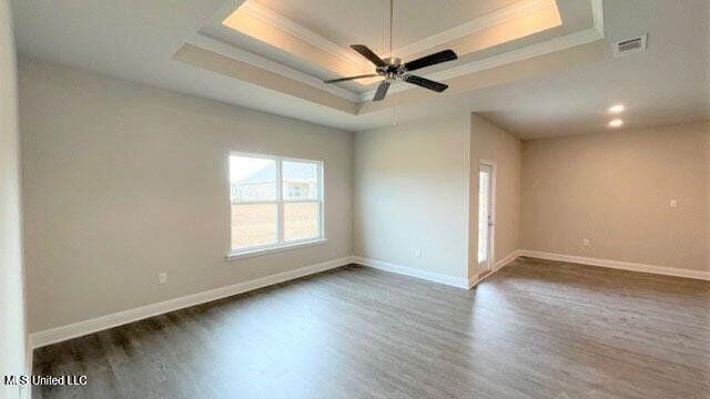 empty room with a raised ceiling, visible vents, dark wood finished floors, and baseboards