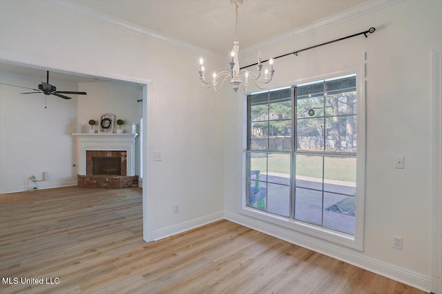 unfurnished dining area featuring light wood-type flooring, ceiling fan with notable chandelier, ornamental molding, and a brick fireplace