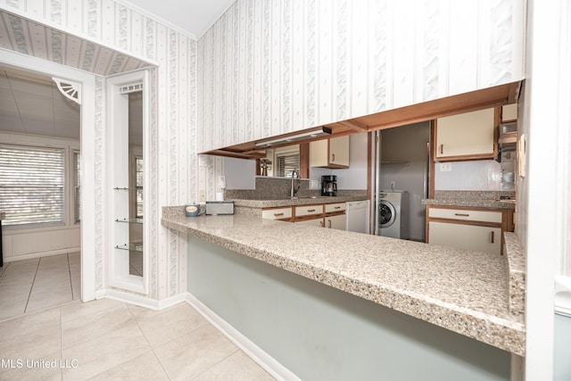 kitchen featuring white dishwasher, sink, light tile patterned floors, kitchen peninsula, and washer / clothes dryer