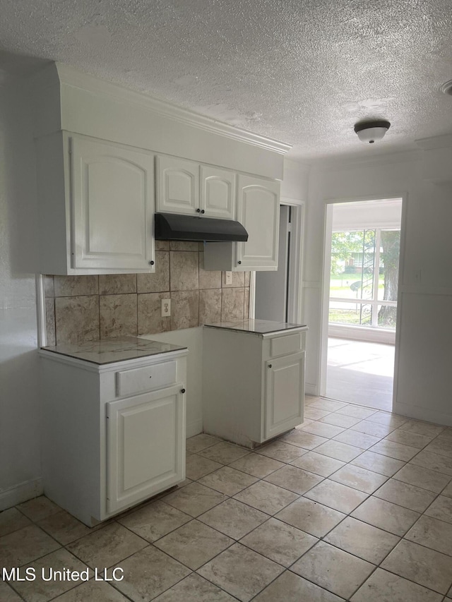 2938 Oak Forest Dr, Jackson, MS 39212 - kitchen featuring white cabinets, backsplash, under cabinet range hood, a textured ceiling, and light countertops