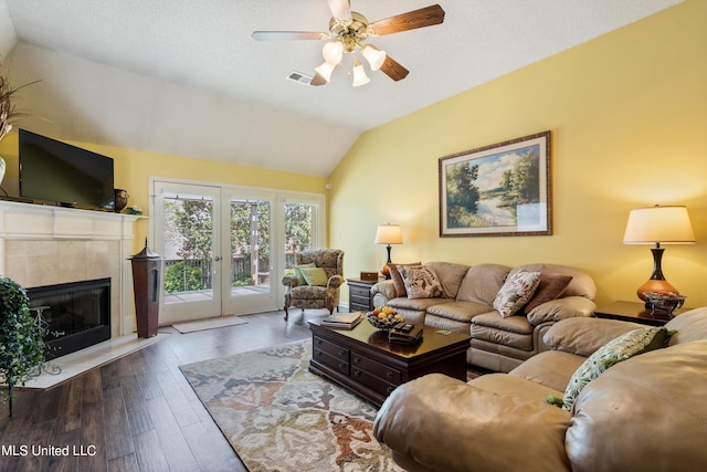 living room featuring a tiled fireplace, ceiling fan, wood-type flooring, vaulted ceiling, and french doors