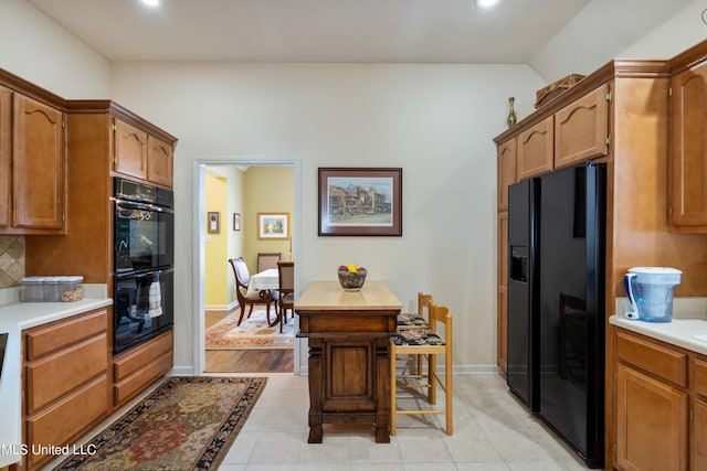 kitchen with black appliances, vaulted ceiling, a kitchen bar, light tile patterned floors, and tasteful backsplash