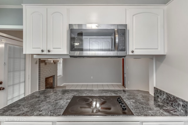 kitchen featuring black electric stovetop, white cabinetry, and a brick fireplace