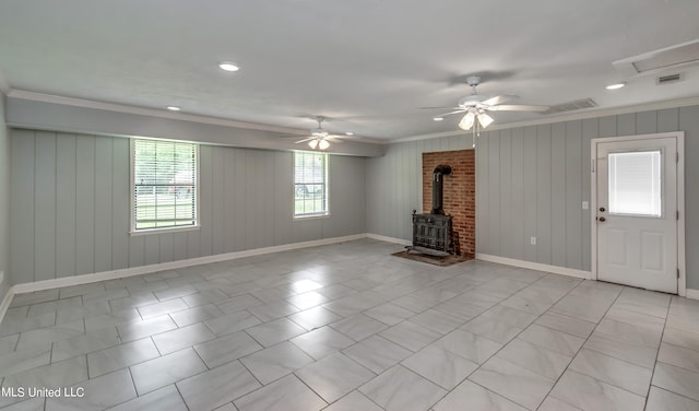unfurnished living room featuring crown molding, wood walls, a wood stove, and ceiling fan
