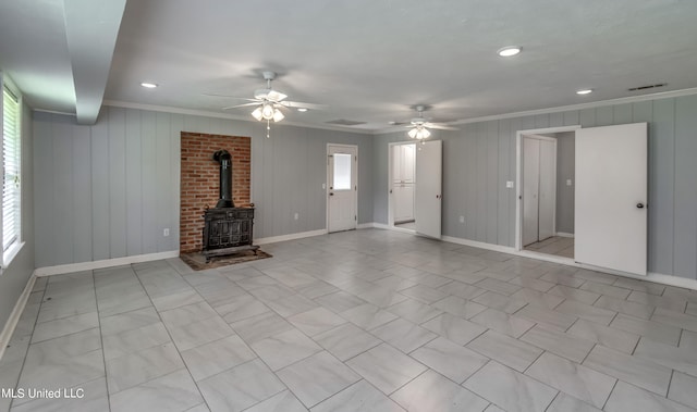 unfurnished living room featuring wooden walls, a wood stove, ornamental molding, and plenty of natural light