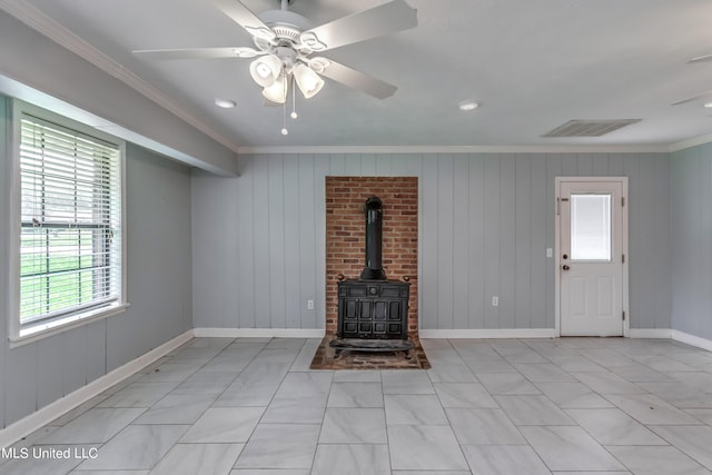 unfurnished living room featuring a wood stove, ornamental molding, wood walls, and ceiling fan